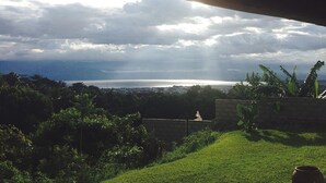 A view from under a roof overlooking a grassy area with a distant body of water and clouds. - Goodlife Residence (Bujumbura)