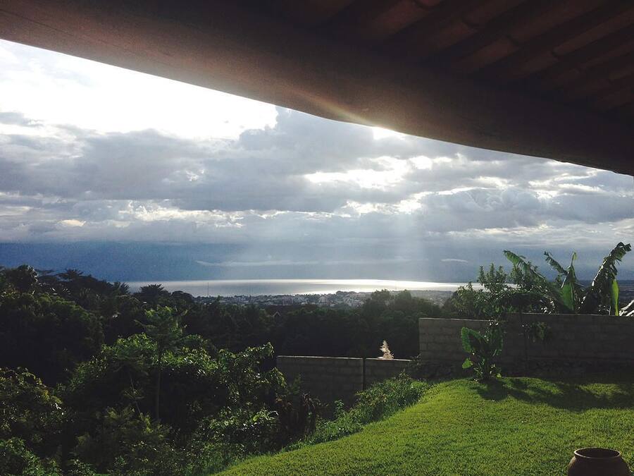 A view from under a roof overlooking a grassy area with a distant body of water and clouds.