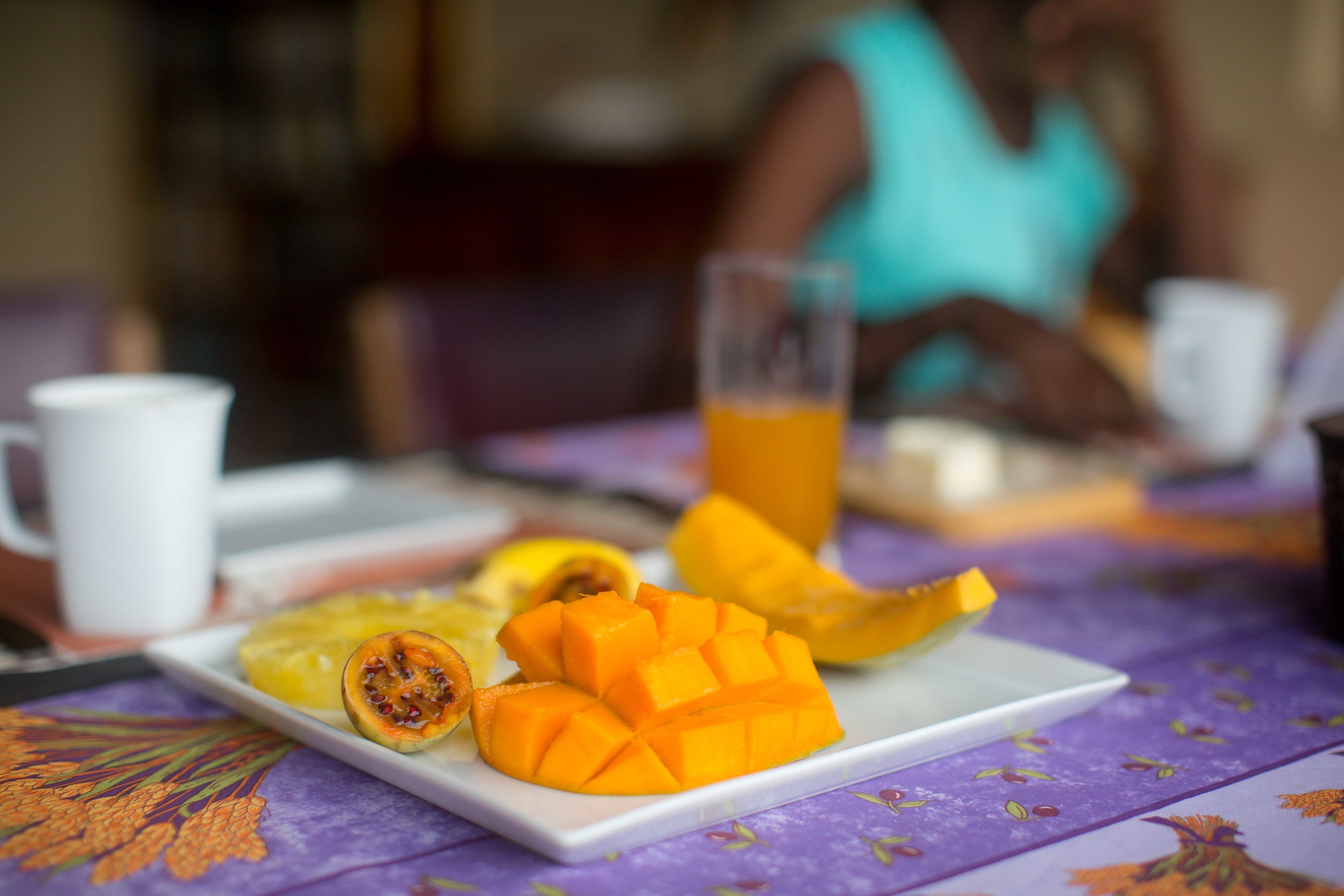 A dining table with a plate of sliced mango and a glass of orange juice.