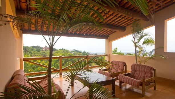 A balcony with a wooden table and two striped chairs, surrounded by potted plants. - Goodlife Residence (Bujumbura)