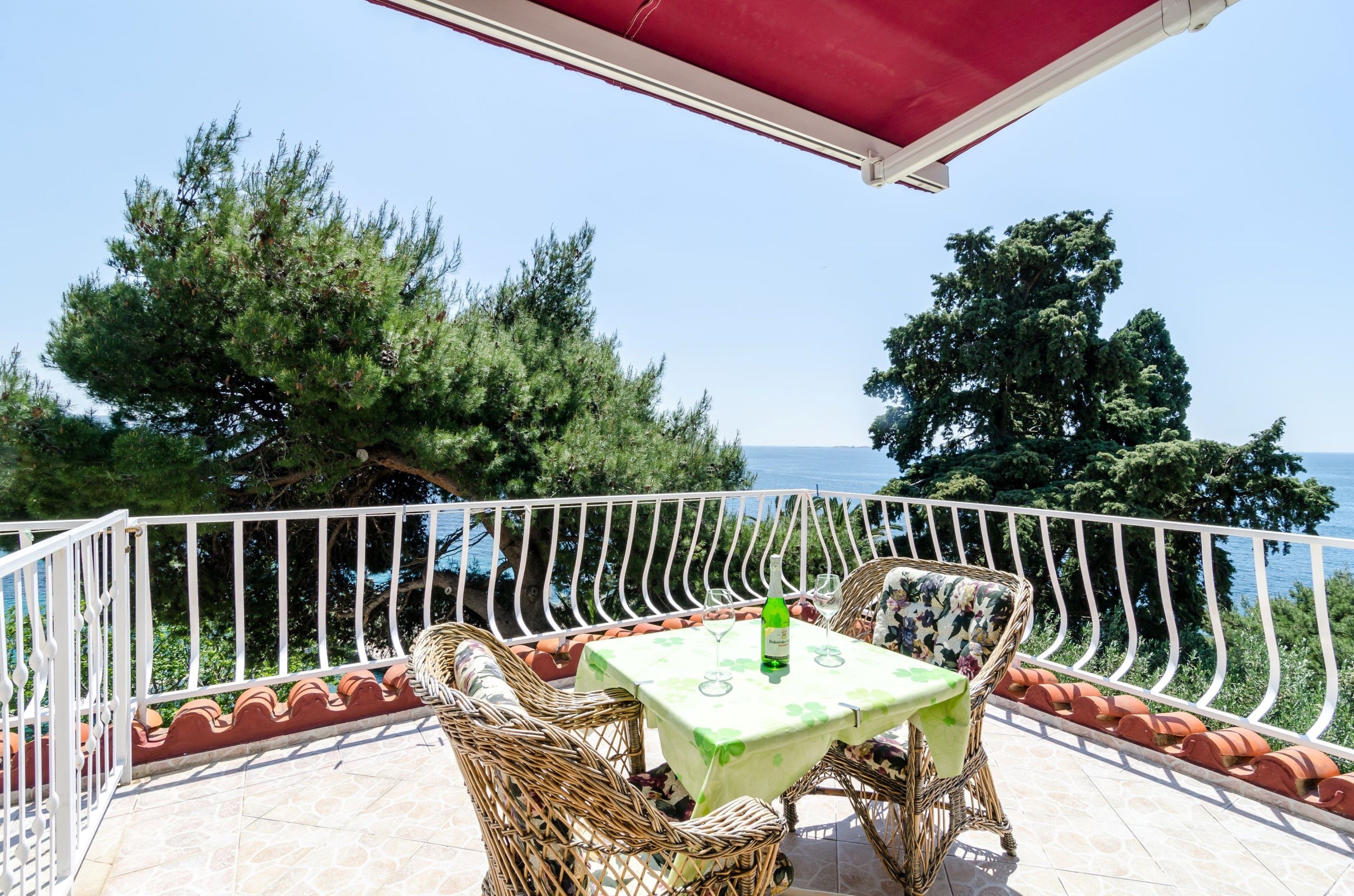 A balcony with wicker furniture, a table with a green tablecloth, and a bottle of wine.