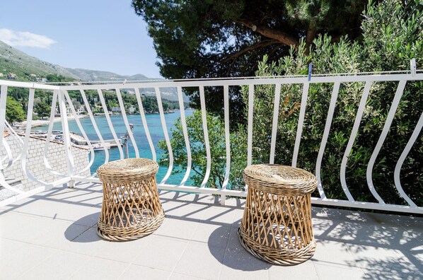 A balcony with wicker stools, a white railing, and a view of a coastal area with boats and greenery. - Guest House Daniela (Zupa dubrovacka)
