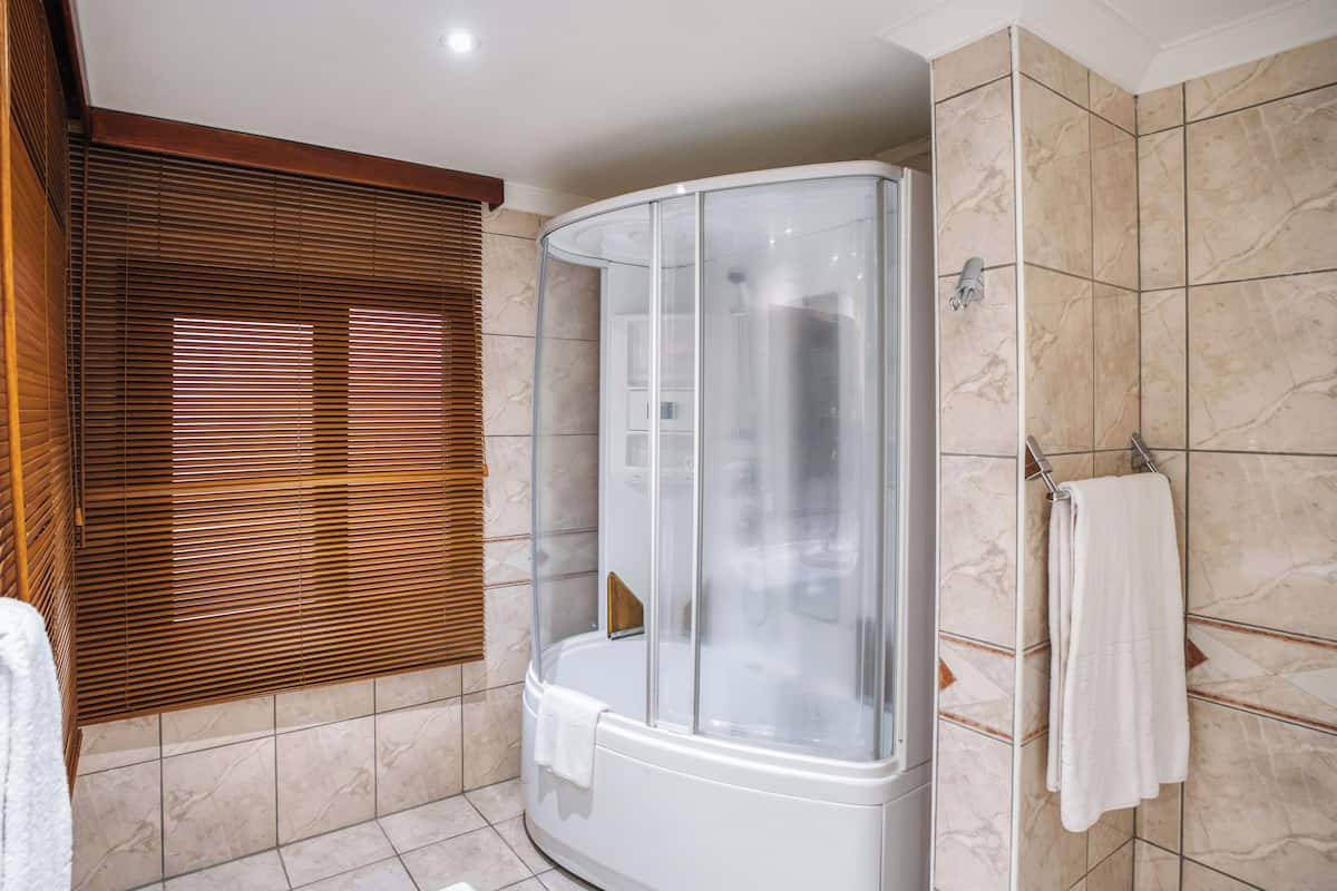 A bathroom with a glass-enclosed shower, wooden blinds, a white towel, and tiled walls.
