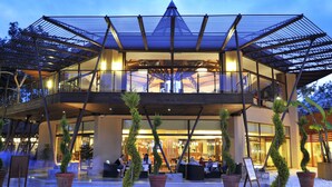 A modern hotel with a glass facade, outdoor seating, and a wooden deck. - Martı Myra - All Inclusive (Kemer)
