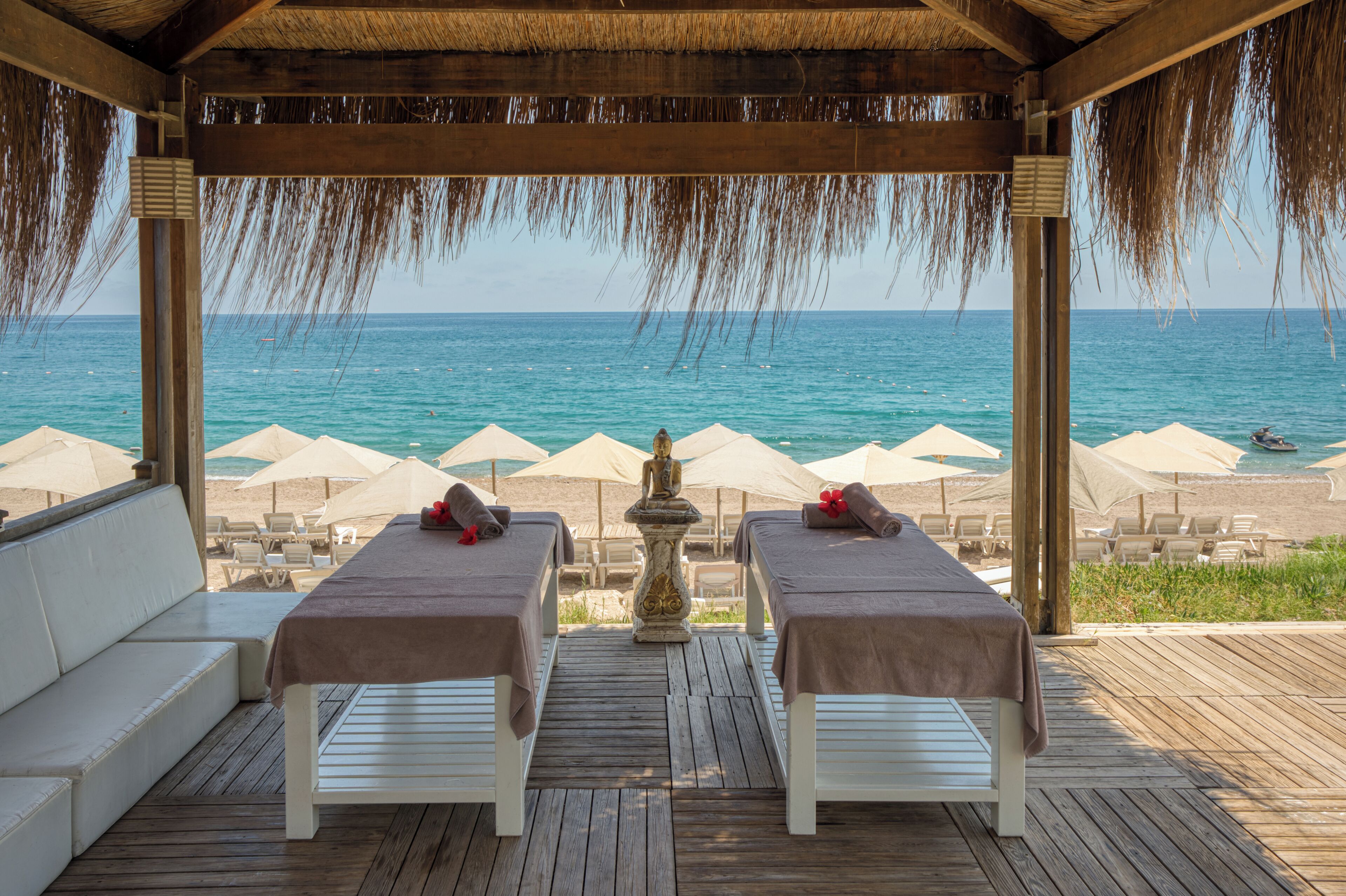 Un spa situé en bord de mer, doté de deux tables de massage, d’une terrasse en bois et de parasols de plage.