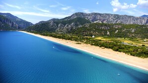 A coastal landscape with a beach, clear blue waters, and mountainous terrain in the background. - Martı Myra - All Inclusive (Kemer)