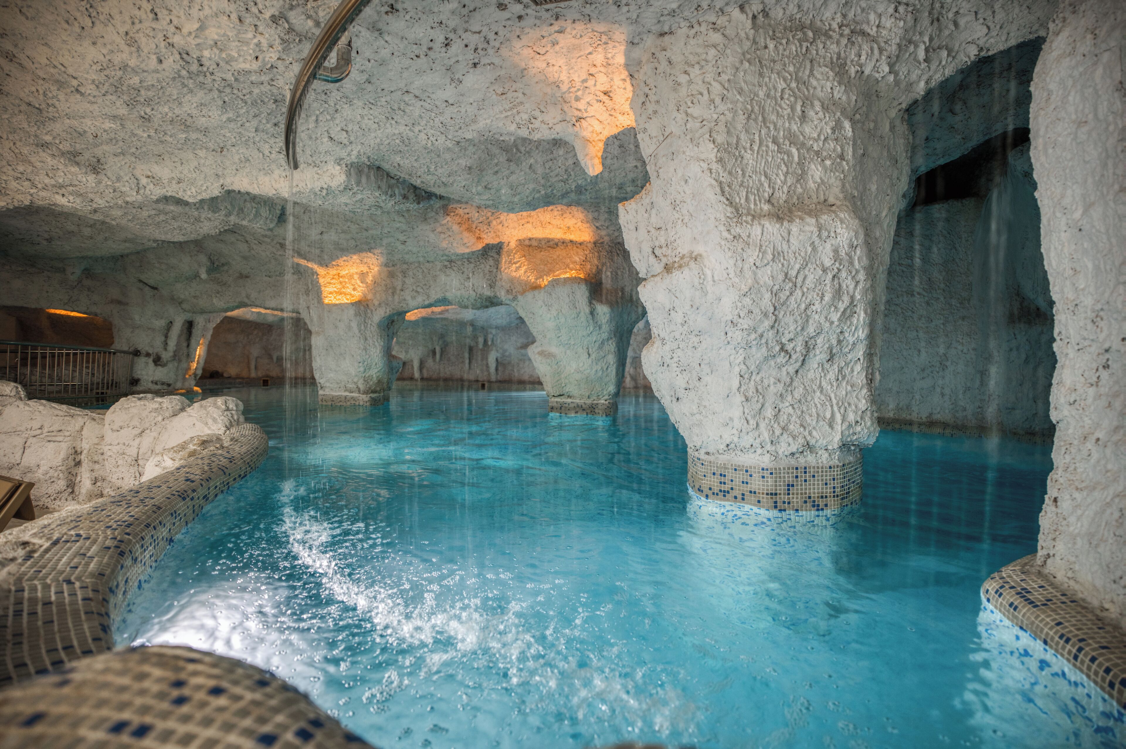Une piscine intérieure à l’eau d’un bleu cristallin, entourée de formations rocheuses et bordée de murs carrelés.