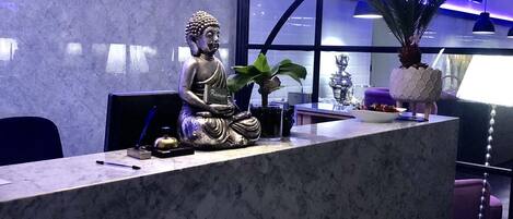 Un mostrador de recepción con una estatua de Buda, una planta en maceta y una lámpara moderna.