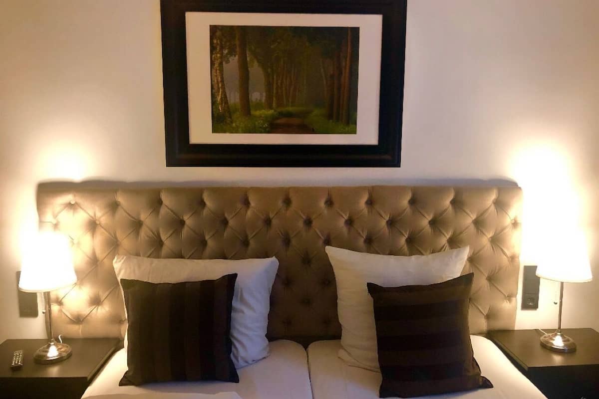 A hotel room with a tufted headboard, a framed picture above the bed, and two bedside lamps.