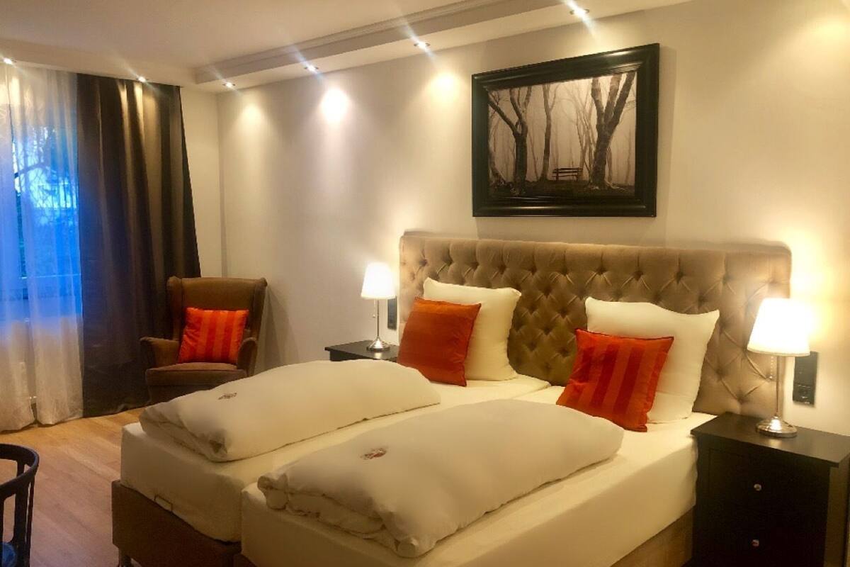 A double bed with white and orange pillows, a tufted headboard, and two bedside tables with lamps.