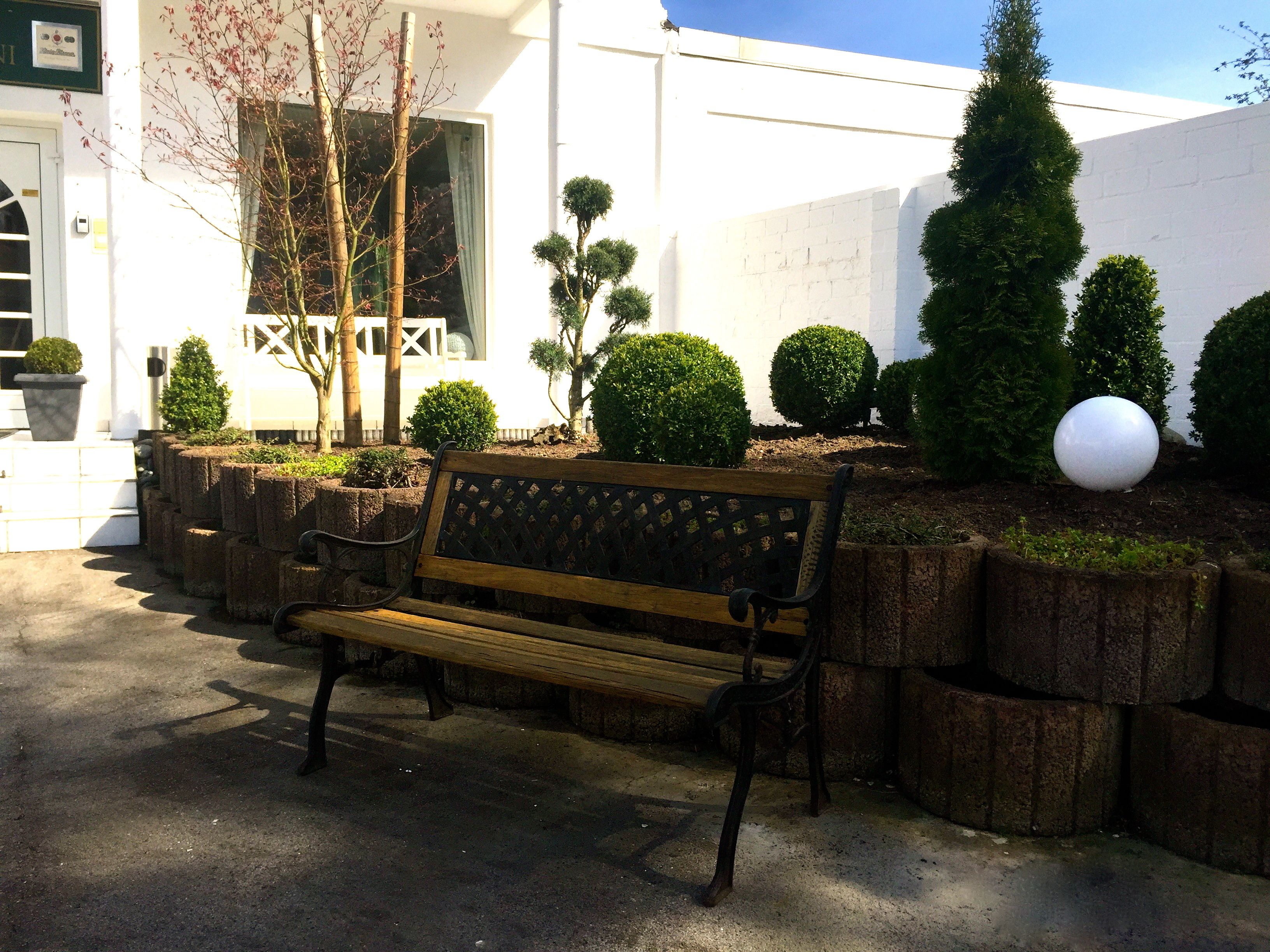Un banco en un jardín con macetas ordenadas y un edificio blanco al fondo.