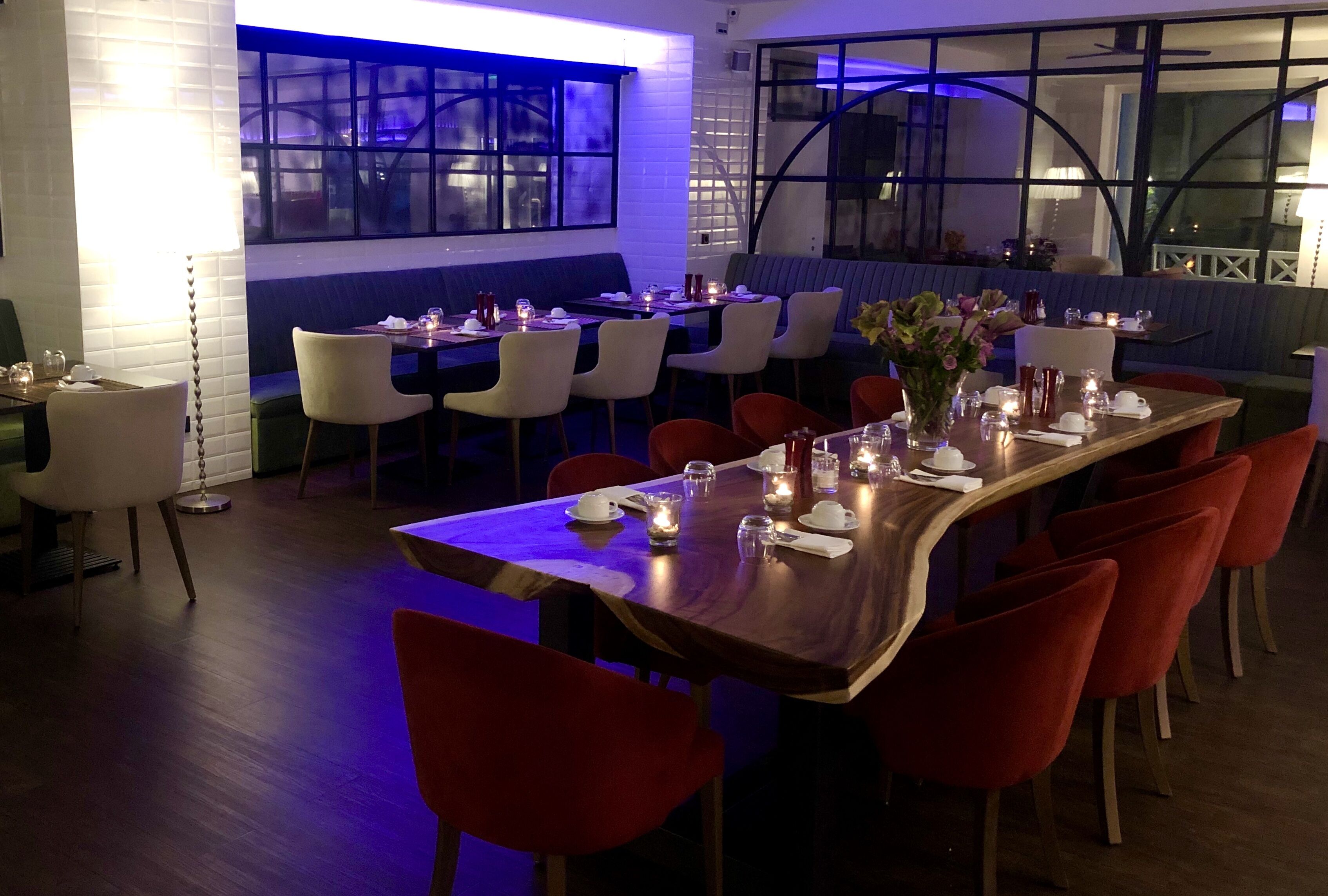 A restaurant with a long wooden table set for dining, surrounded by red and white chairs.