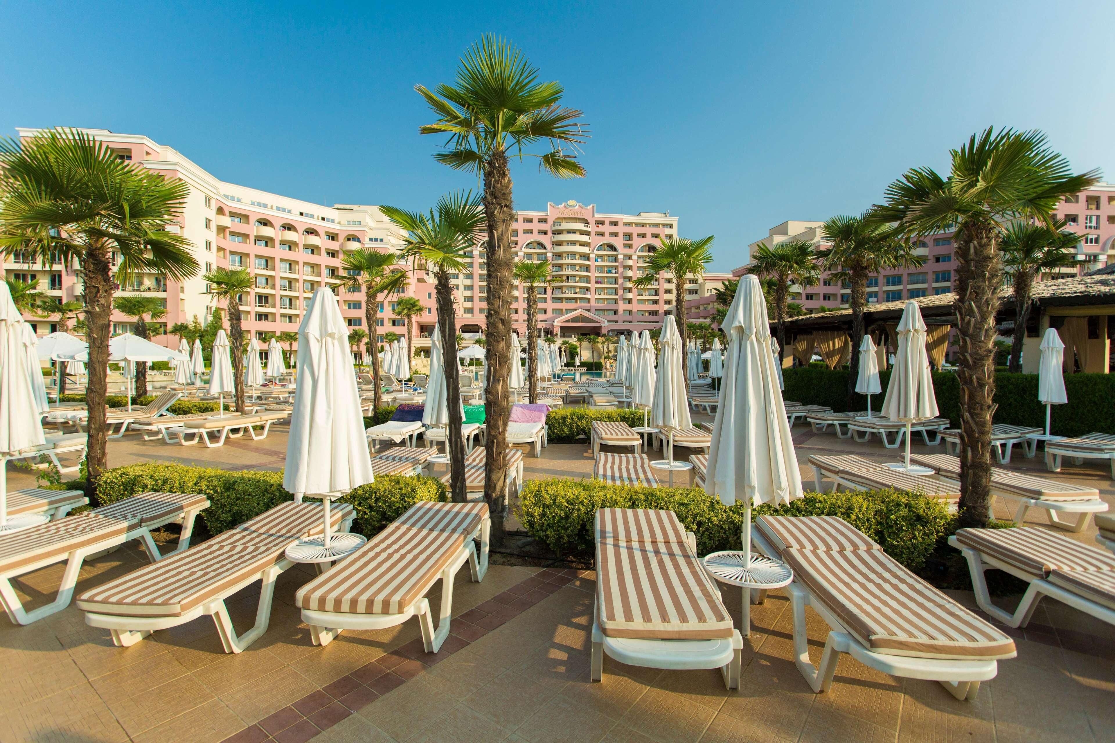 A resort with multiple lounge areas, palm trees, and a large hotel building in the background.