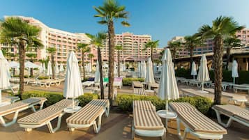 A resort with multiple lounge areas, palm trees, and a large hotel building in the background.