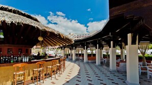 Un área de bar al aire libre con techo de paja, sillas de mimbre y piso de baldosas.
