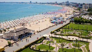 Un paisaje urbano costero con playa, paseo marítimo y jardines ajardinados.