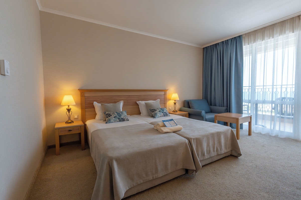 Une chambre d’hôtel avec un grand lit, deux tables de chevet avec des lampes, un canapé et une vue sur l’extérieur.