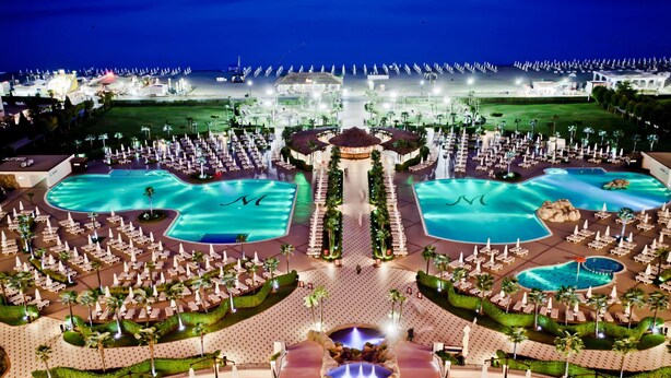 Un resort con varias piscinas, tumbonas y una fuente central.