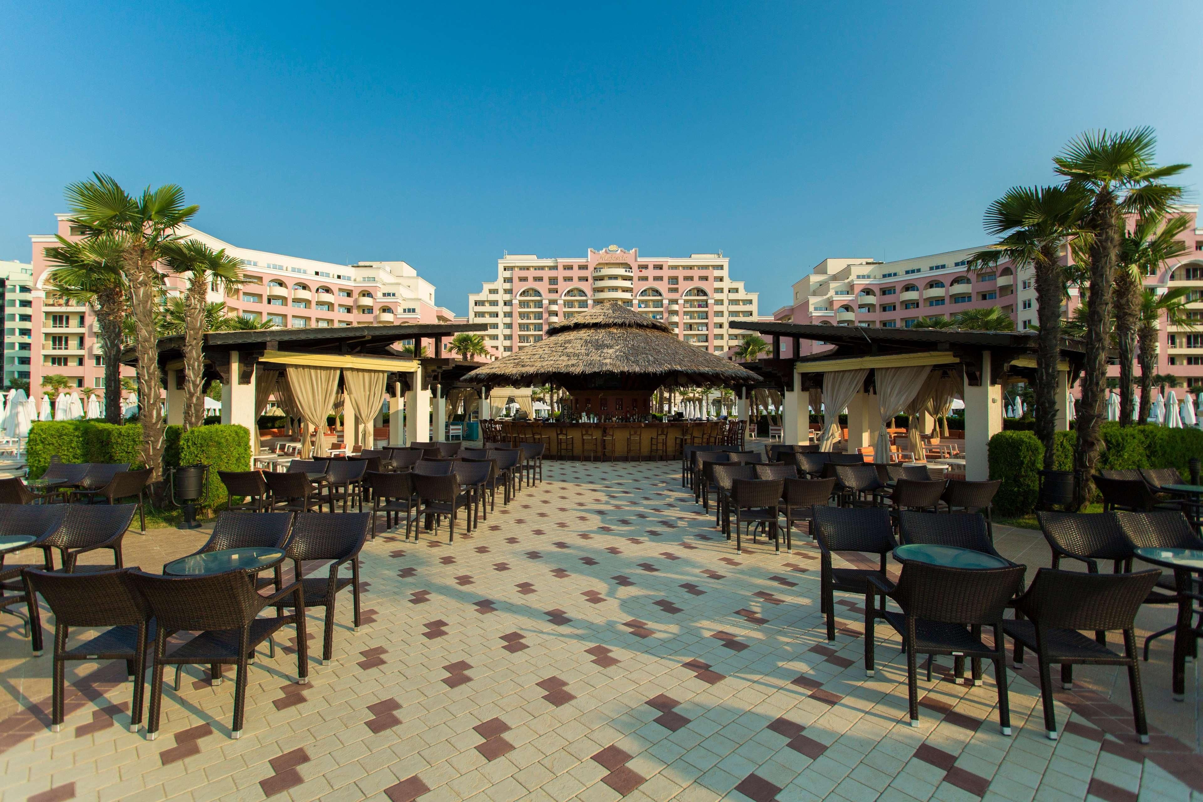 A hotel courtyard with outdoor seating, a central bar, and a thatched-roof structure.