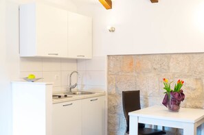 A kitchen with white cabinets, a sink, and a stone wall. - Split Oasis Apartments (Split)