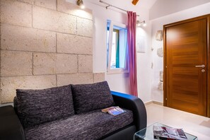 A room with a sofa, a glass table, a wooden door, and a window with a curtain. - Split Oasis Apartments (Split)