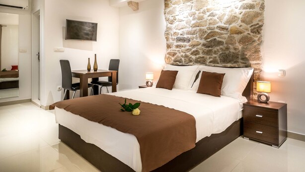 A bedroom with a stone accent wall, a bed with brown bedding, a desk with chairs, and bedside lamps.