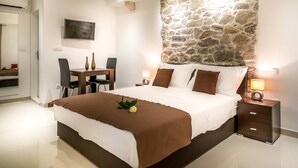 A bedroom with a stone accent wall, a bed with brown bedding, a desk with chairs, and bedside lamps.