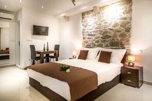 Un dormitorio con pared de piedra decorativa, cama con ropa de cama marrón, escritorio con sillas y lámparas de noche.