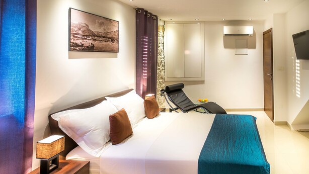 A hotel room with a bed, a nightstand with a lamp, a chair, a TV, and a painting on the wall.