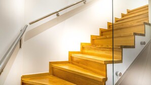 A wooden staircase with a glass railing and metal handrail.