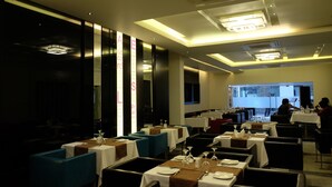 Interior moderno de restaurante con mesas dispuestas para comer, asientos tipo banca acolchados en azul y una gran pantalla de proyección al fondo.