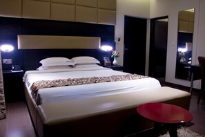 A hotel room with a large bed, bedside lamps, a small table, and a mirror. - D'more Dhaka Hotel & Resort (Dhaka)