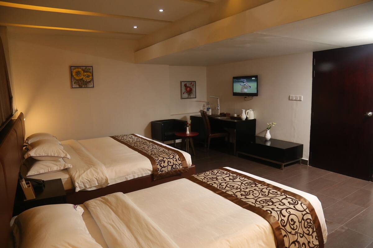 Una habitación de hotel con dos camas, un escritorio, una silla, un televisor y una puerta.