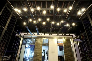 A modern building with a glass facade, a stone column, and a series of lights on the ceiling.