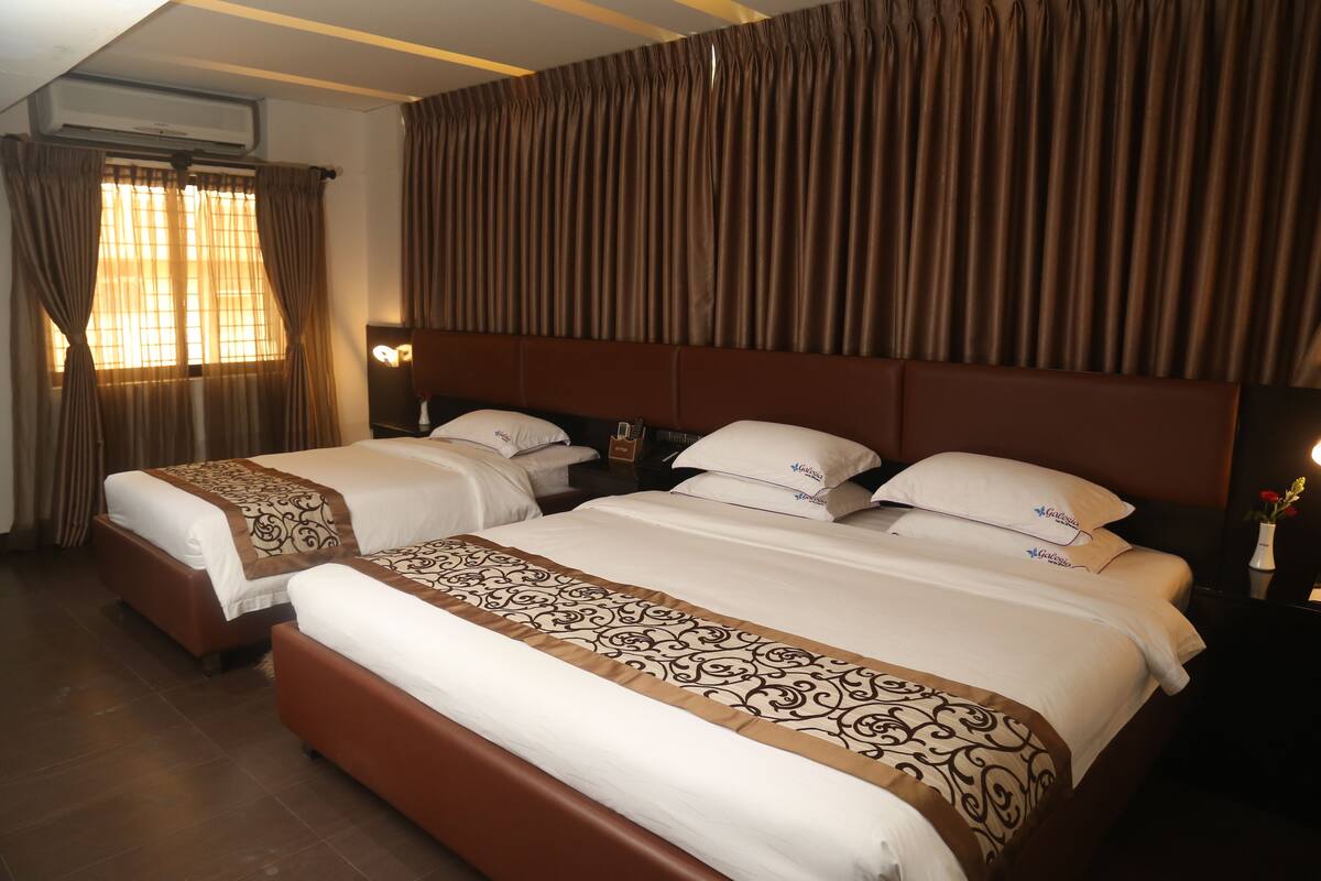 Habitación de hotel con dos camas, un ventanal grande con cortinas y un cabecero con fondo de cortina.