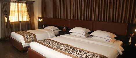 A hotel room with two beds, a large window with curtains, and a headboard with a curtain backdrop.