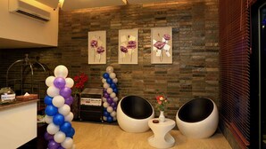 Zona de recepción con pared de piedra, obras de arte enmarcadas, un arco de globos y asientos modernos.
