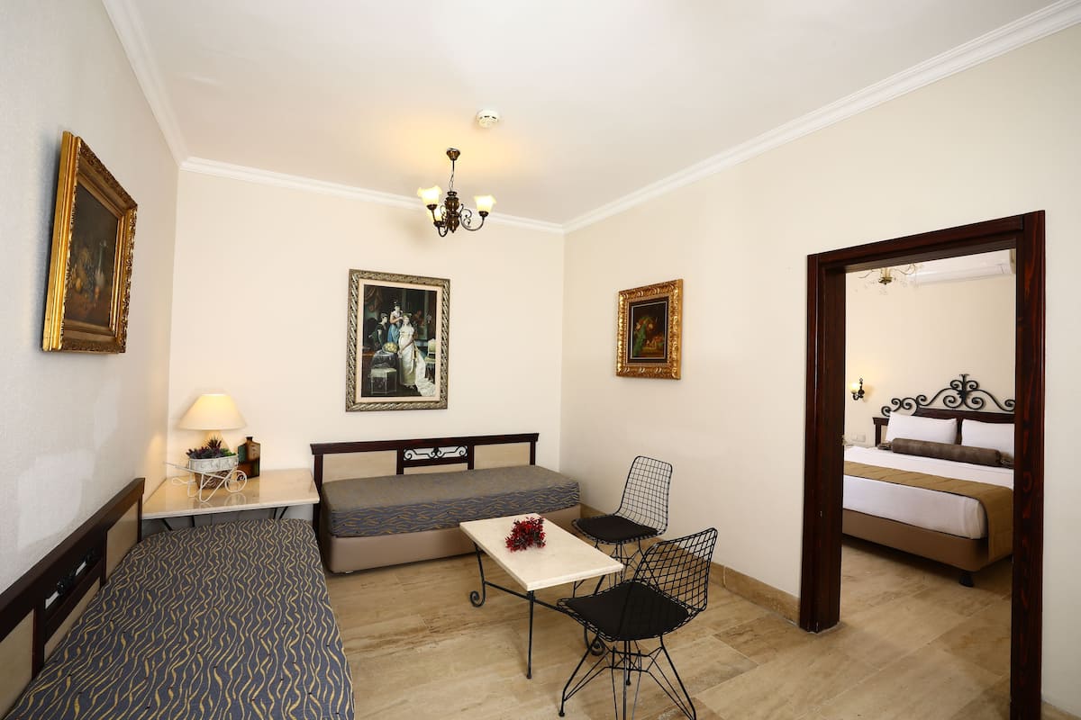 A room with a bed, a sofa, a table, and two chairs. There are framed pictures on the walls and a chandelier.