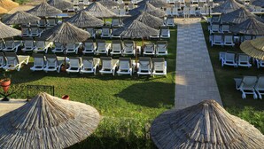 A beachside resort with rows of sun loungers under thatched umbrellas, a pier extending into the sea, and a clear view of the coastline. - Cactus Fleur Bay Resort - All inclusive (Bodrum)