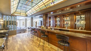 Una zona de bar con mostrador de madera, taburetes y un techo de vitrales.