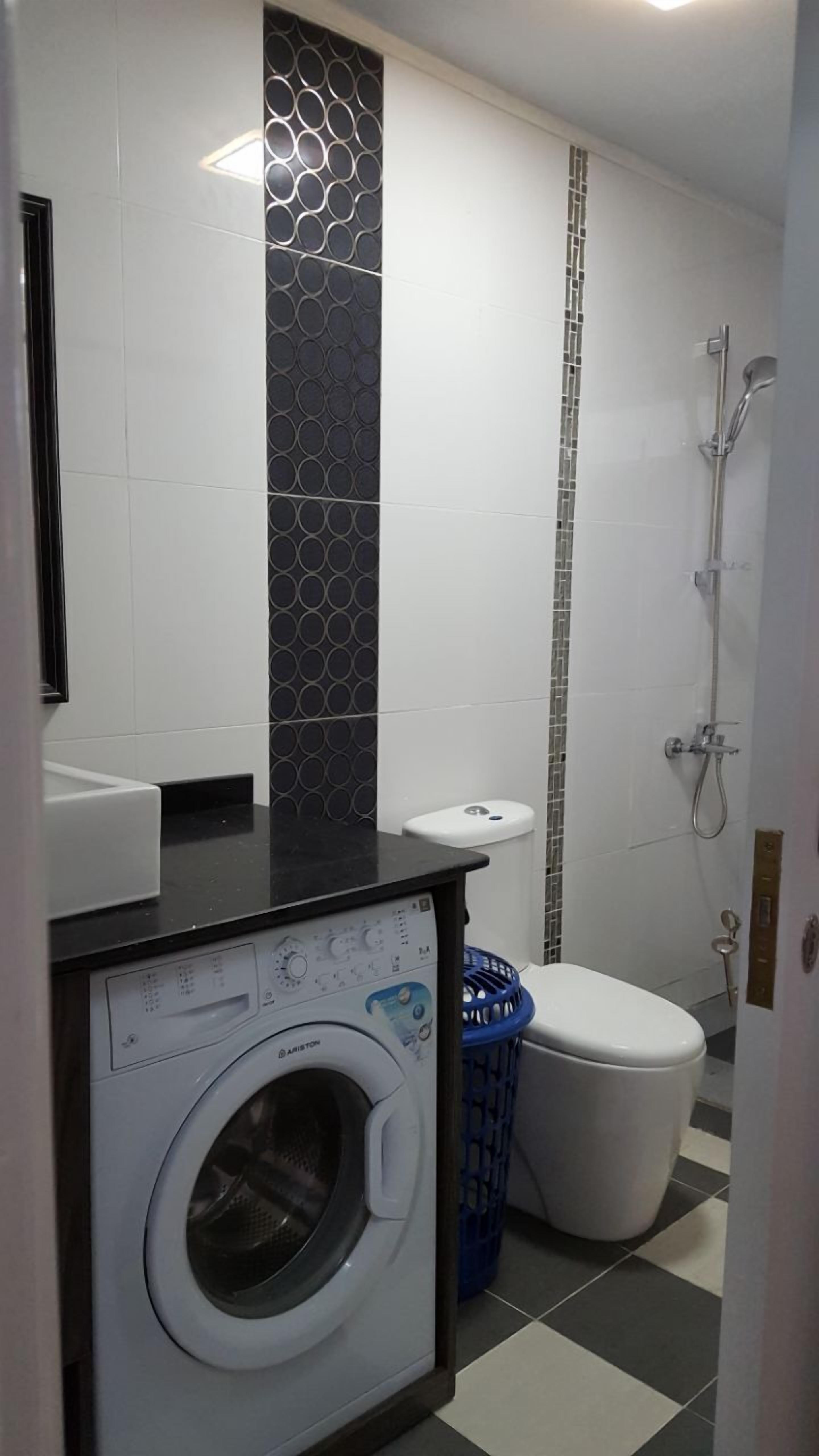 A compact bathroom with a washing machine, toilet, and shower.