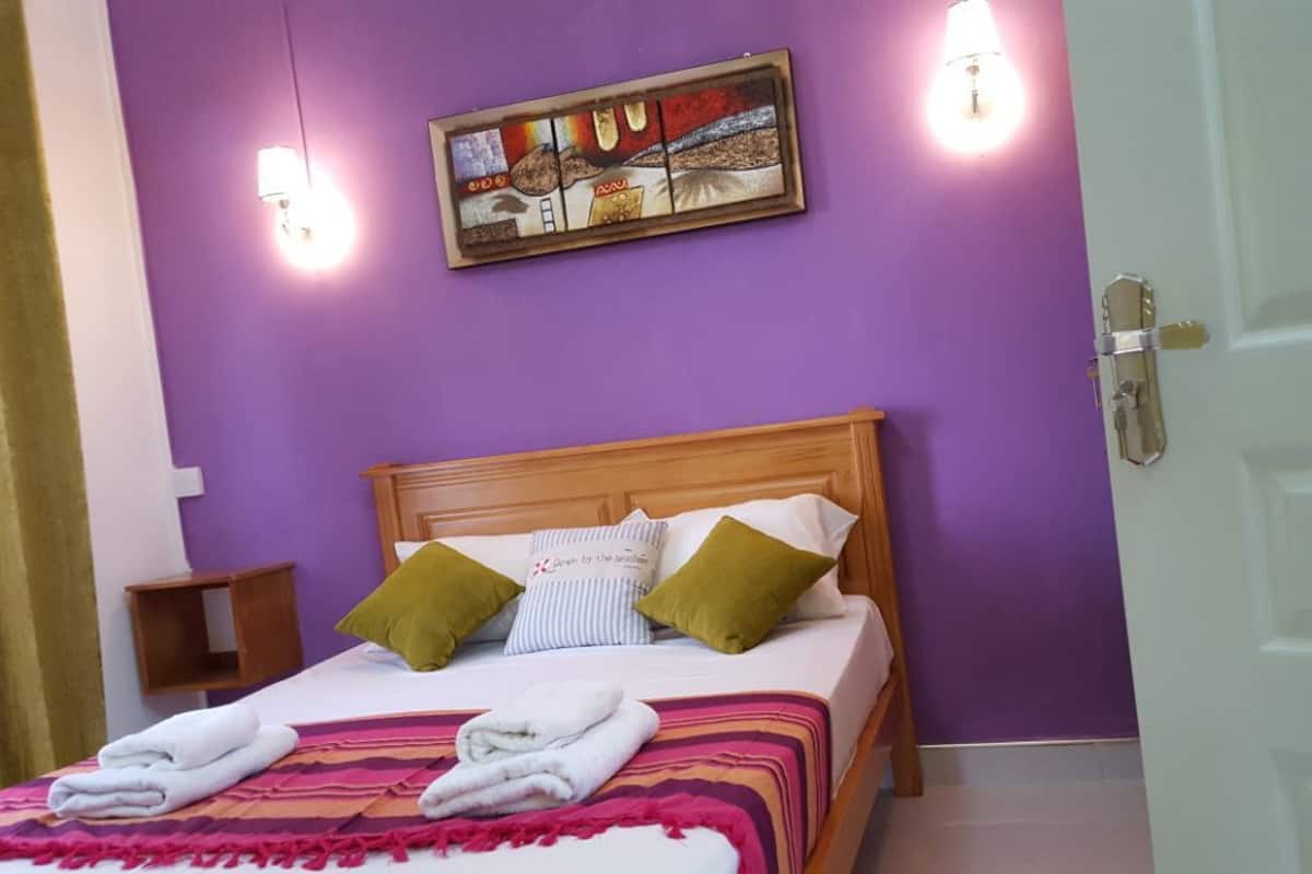 A bedroom with a wooden bed, purple walls, and a painting above the bed.