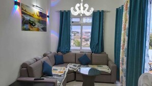 A living room with a sofa, a small table, a chandelier, and a view through a window.