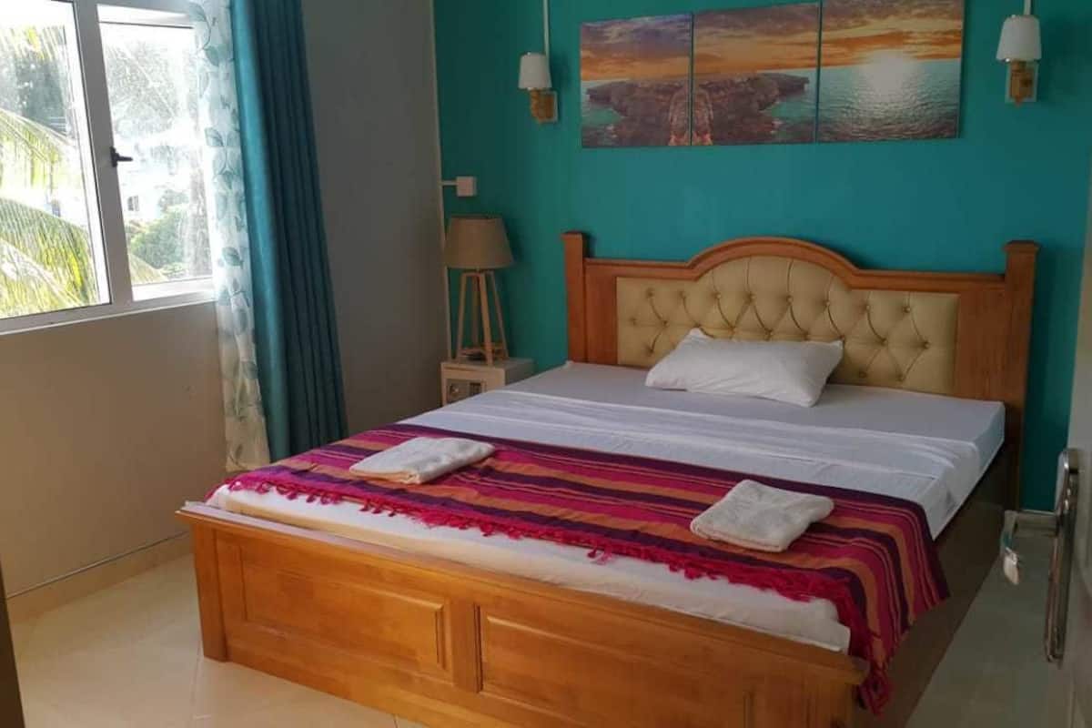 A bedroom with a wooden bed, a view of greenery outside, and a painting on the wall.