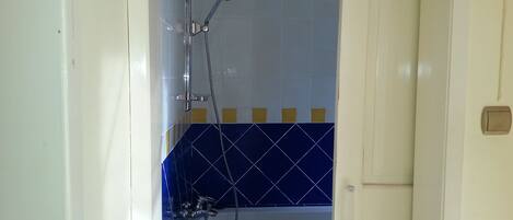 A shower with a handheld showerhead and a wall-mounted faucet.