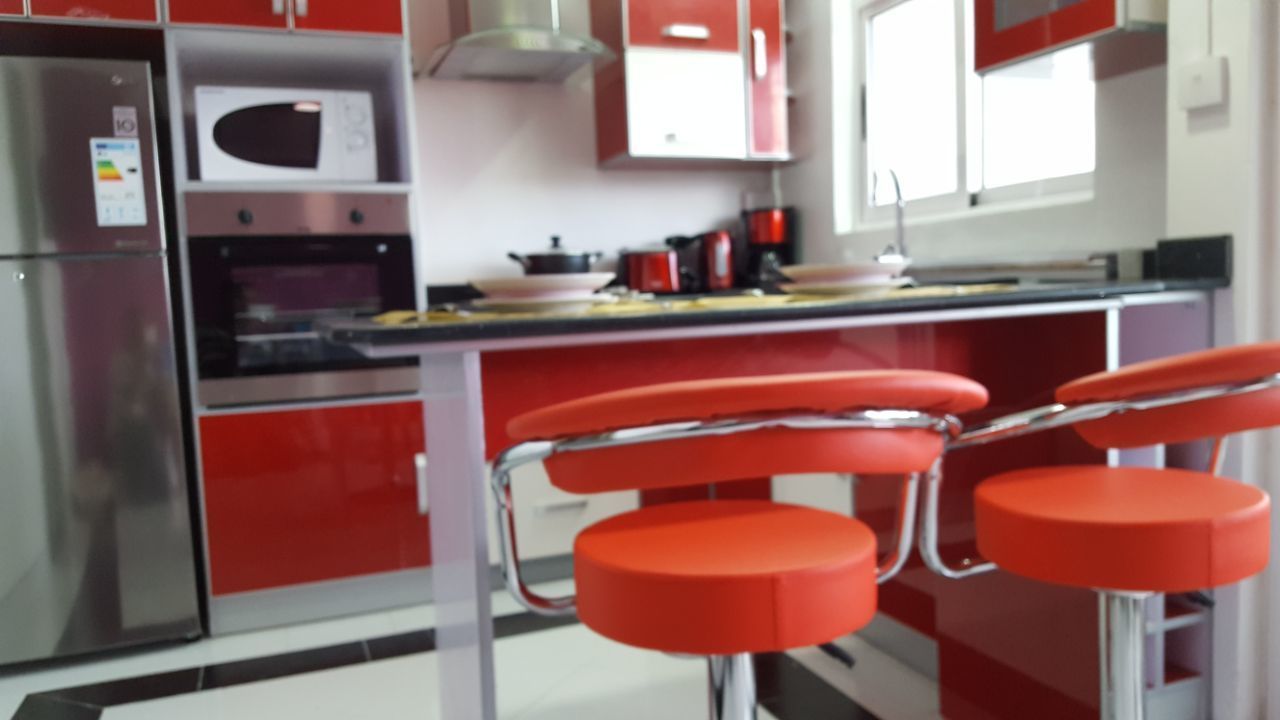 A kitchen with red cabinets, a stainless steel refrigerator, a microwave, and a stove. There are two red bar stools.