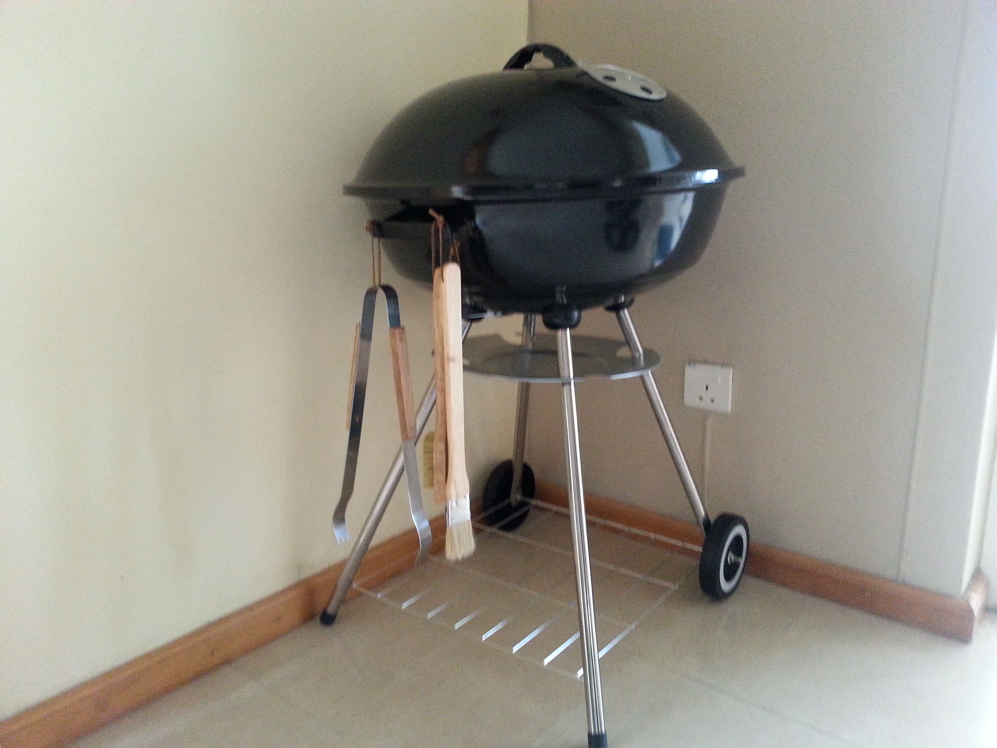 A portable barbecue grill with a metal stand and wheels, placed indoors against a wall.