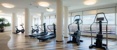 A spacious gym with various exercise equipment, large windows, and a modern design.
