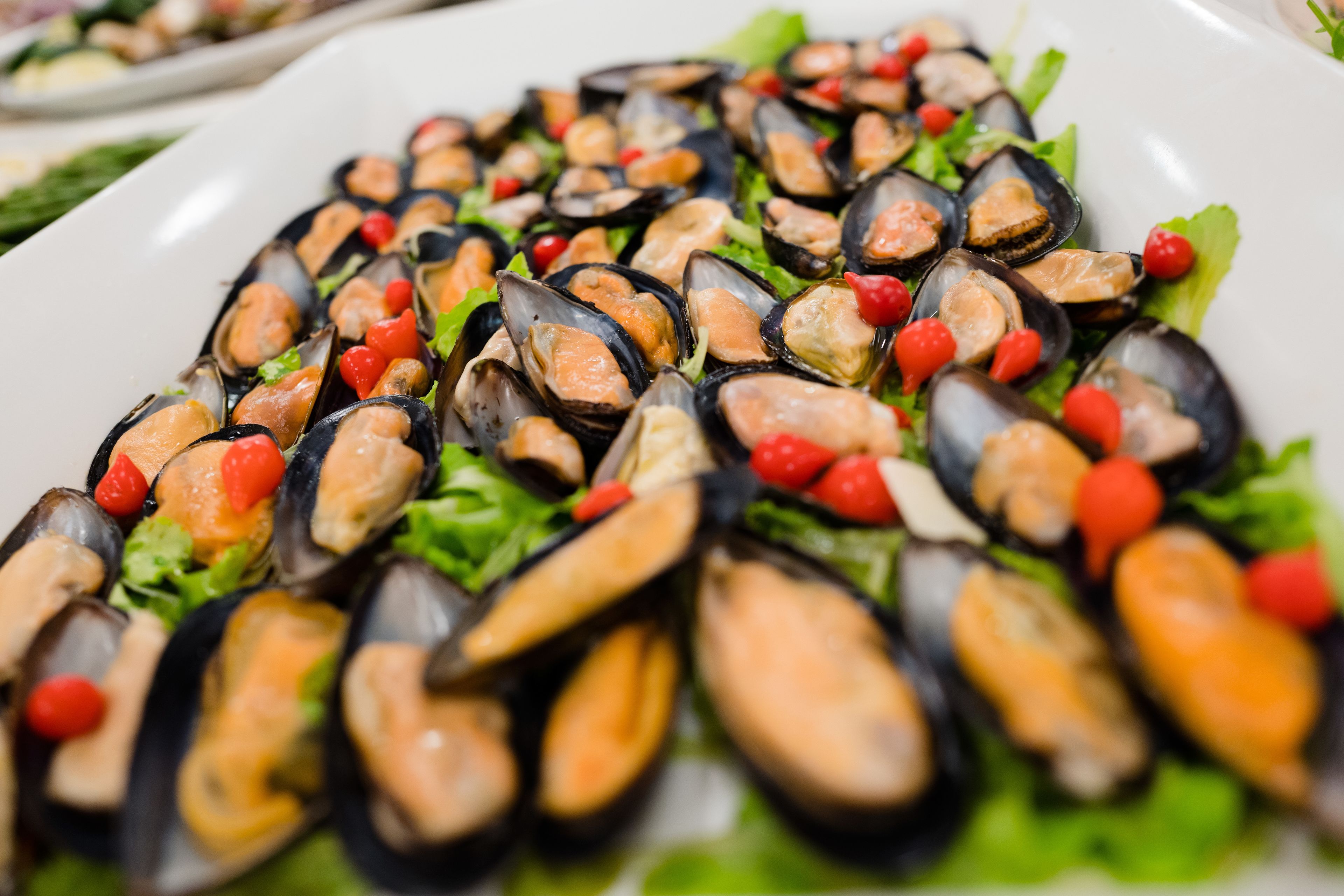 Une assiette de moules, agrémentée de grains de poivre rouge et de feuilles de laitue verte.