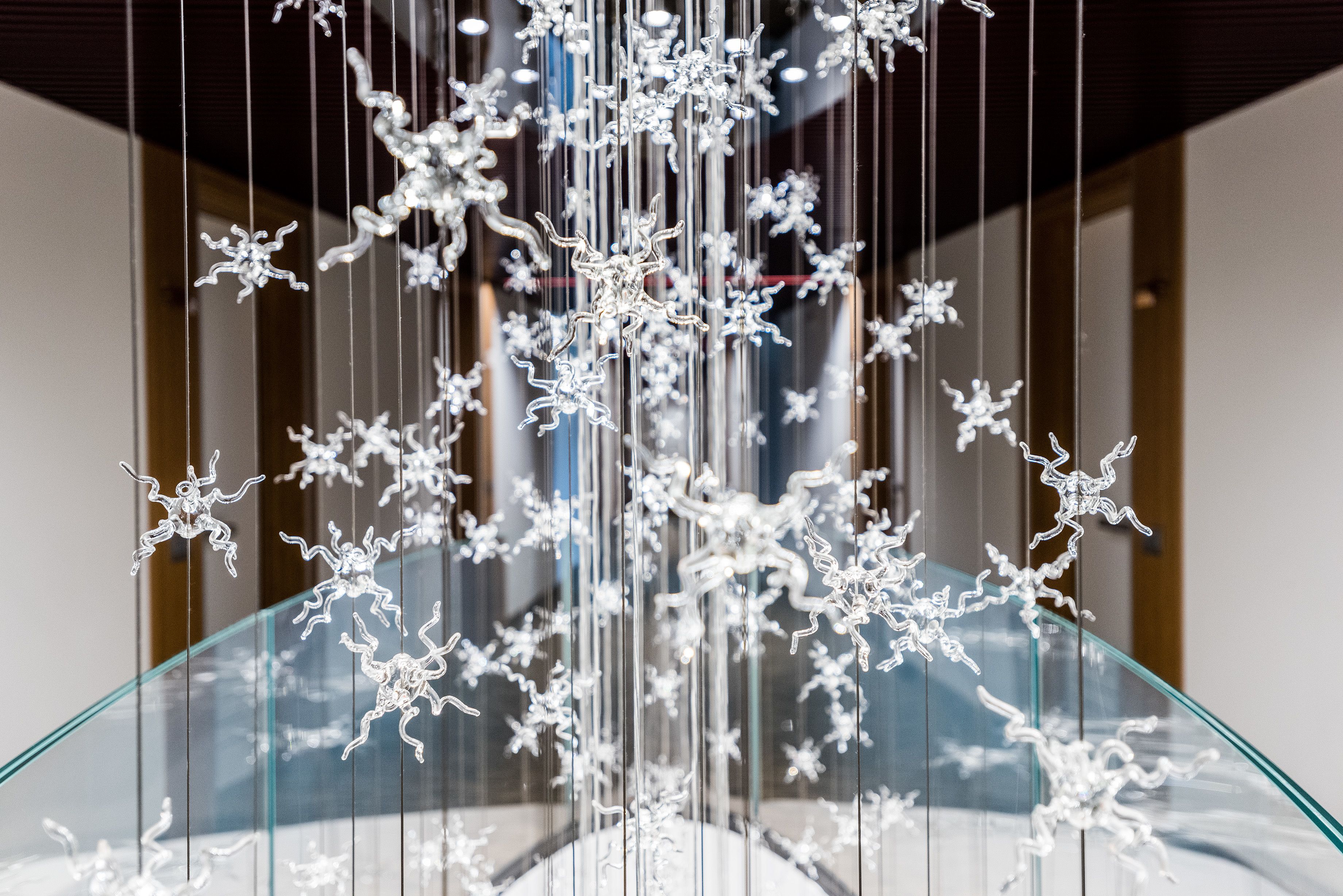 A modern interior with a glass staircase and hanging metallic sculptures.